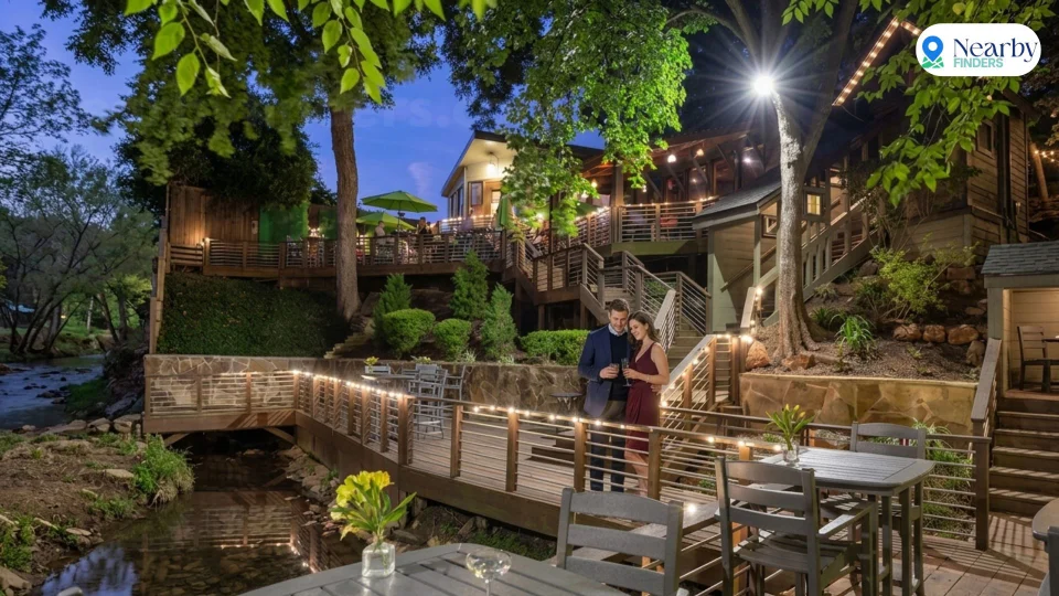 Romantic restaurants for couples in Houston: A romantic couple standing on the wooden deck walkway next to a peaceful stream during an evening date night at Rainbow Lodge Houston